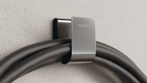 Easee U-Hook in chrome holding looped black EV charging cable on textured plaster wall, wall-mounted cable storage